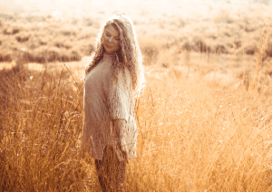 Foto van een vrouw die zich zelfverzekerd en energiek voelt, met open armen in een geel veld